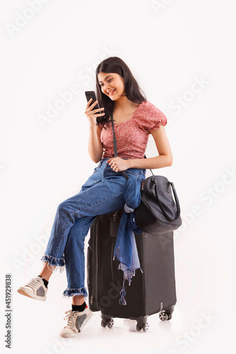Photography A young travelling woman sitting on  her baggage looking at her mobile phone