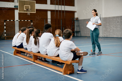 Foto Happy physical education teacher talks to her students during class at elementary school gym
