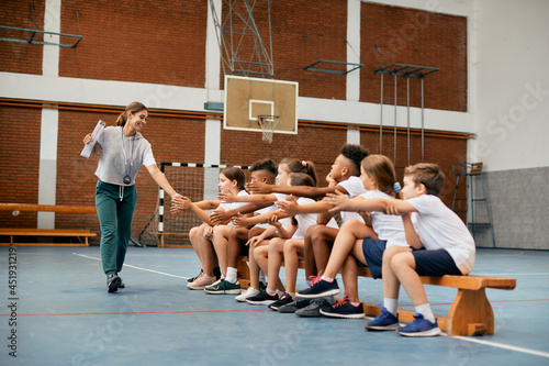 Happy sports teacher greets with group of elementary students during PE class at school gym. photo