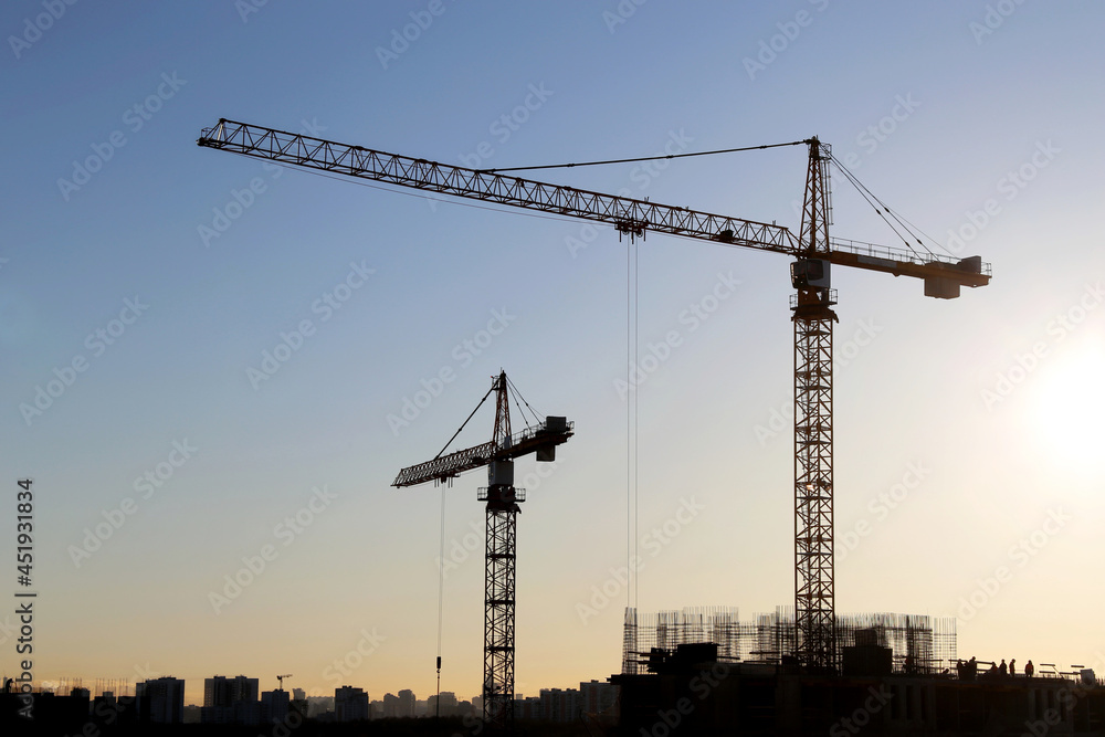 Tower cranes and construction site on sunrise background. Housing development, unfinished buildings in city