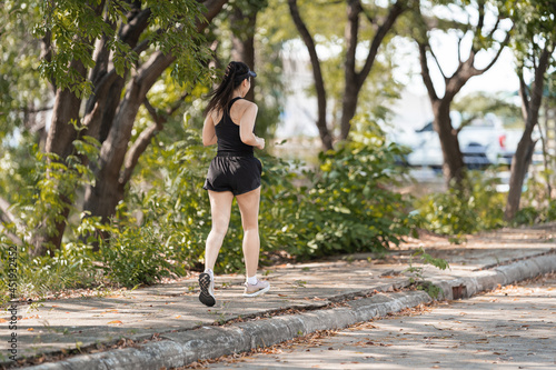 Fototapeta Naklejka Na Ścianę i Meble -  A healthy happy Asian woman runner in black sport outfits jogging in the natural city park under evening sunset