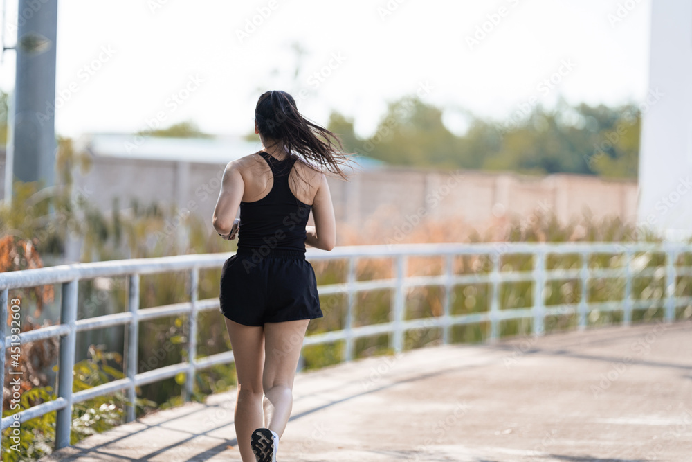 A healthy happy Asian woman runner in black sport outfits jogging in the natural city park under evening sunset A healthy happy Asian woman runner in black sport outfits jogging in the natural city park under evening sunset
