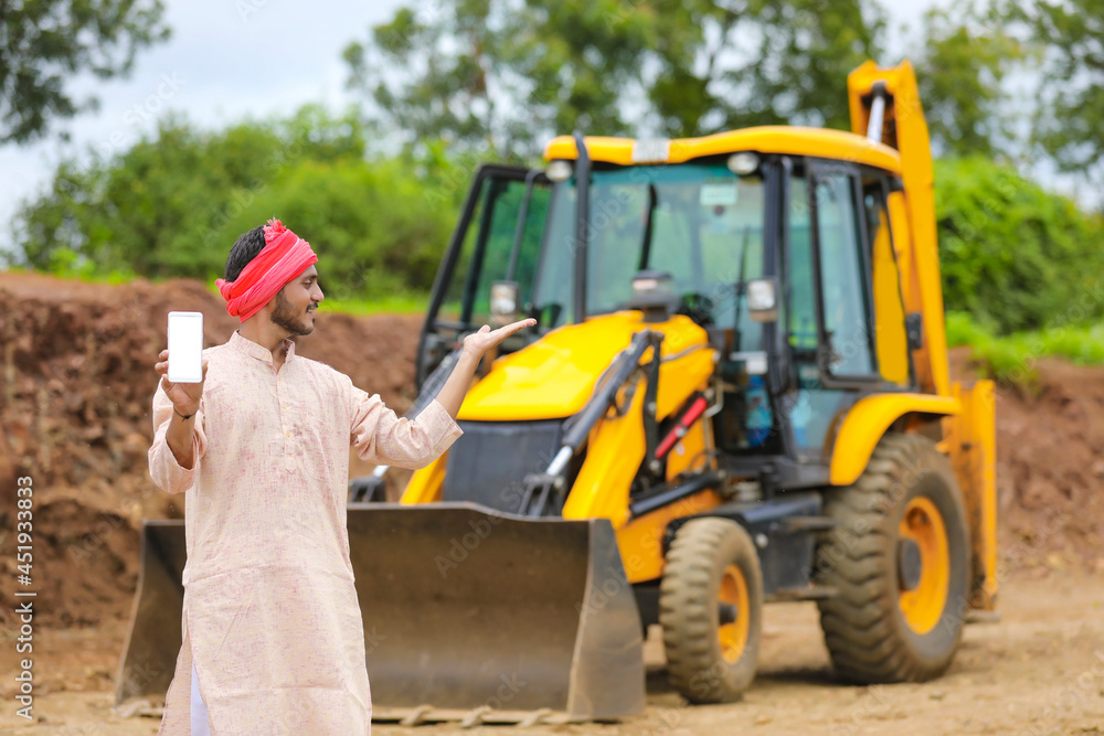 Indian farmer showing smartphone with his new earth mover machine equipment Indian farmer showing smartphone with his new earth mover machine equipment
