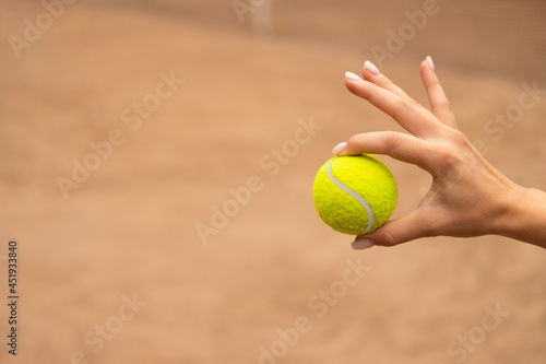 Hand holding a tennis ball isolated on a colored background. © Илья Мышенков