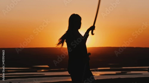 Young woman in a hoodie swinging with a blade on late orange sunset photo