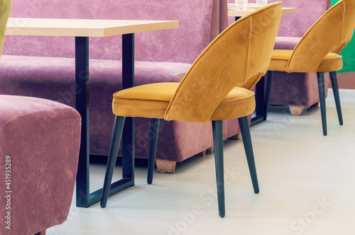 A row of tables with soft comfortable violet chairs for visitors to the food court of a modern shopping center