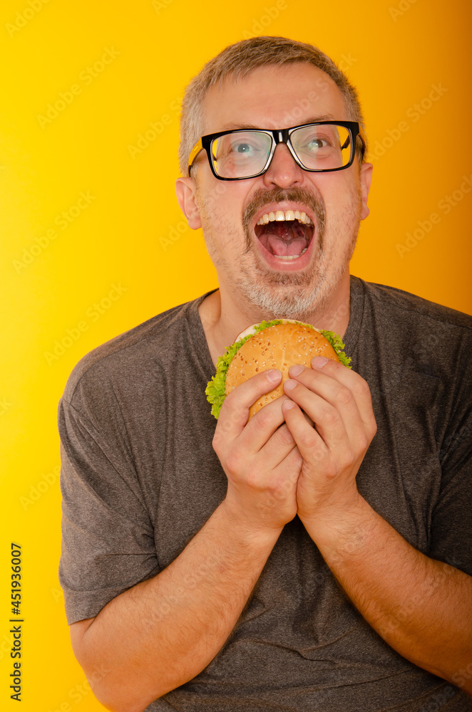 Fabulous at any age, vegetarian food concept. Portrait of fashionable 60-year-old man in stylish sweater posing with burger. Trendy haircut, glossy grey hair. Close up. Copy-space. Studio shot
