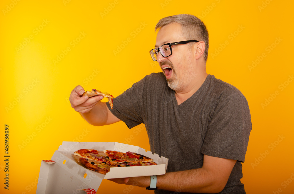 Funny hungry light skinned man, grandpa biting pizza, eating junk food, standing against yellow studio background. European man is enjoying a hamburger. Unhealthy eating and overeating Funny hungry light skinned man, grandpa biting pizza, eating junk food, standing against yellow studio background. European man is enjoying a hamburger. Unhealthy eating and overeating