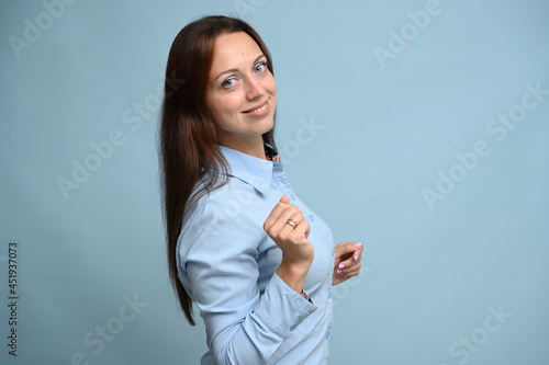 young woman in a blue shirt with a smile stands on a blue background