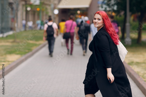 European plus size woman walking outdoor street city. Young red pink haired body positive girl. © primipil