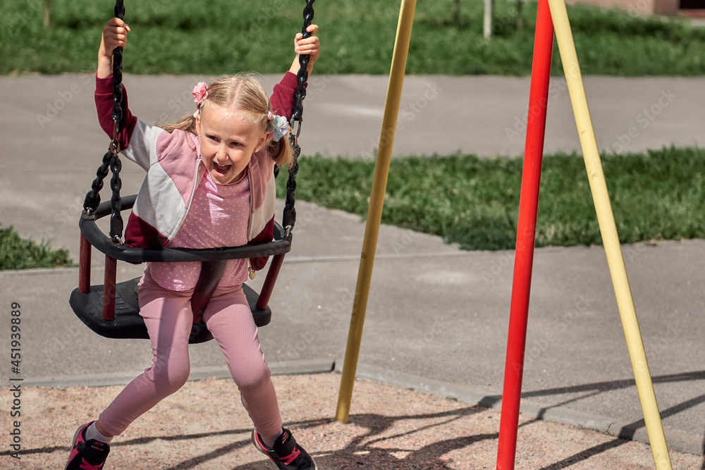 Kids play on the playground. Happy laughing girl have fun swinging and climbing outdoor
