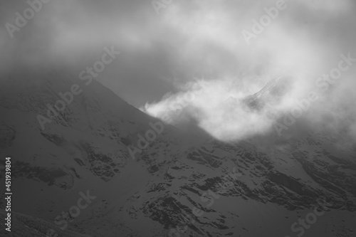 Alpine view in Tatra Mountains, Poland. Dark winter sky over snowy ridge. Dramatic cloudscape. Selective focus on the rocks, blurred background.
