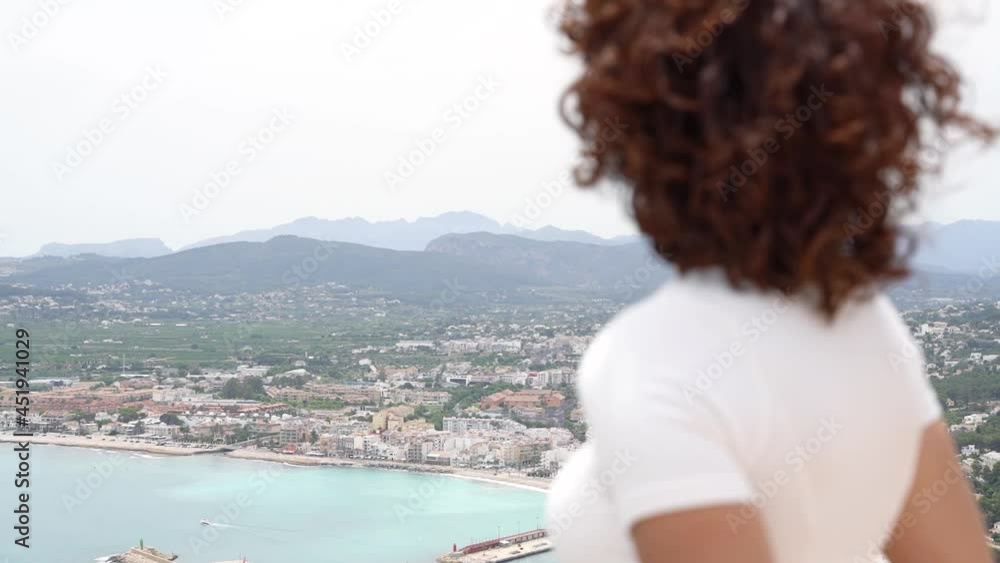 Panoramic view with selective focus from curly woman sightseeing to Javea landscape. Happy woman traveling in spanish coast city of Javea. Panoramic view with selective focus from curly woman sightseeing to Javea landscape. Happy woman traveling in spanish coast city of Javea.
