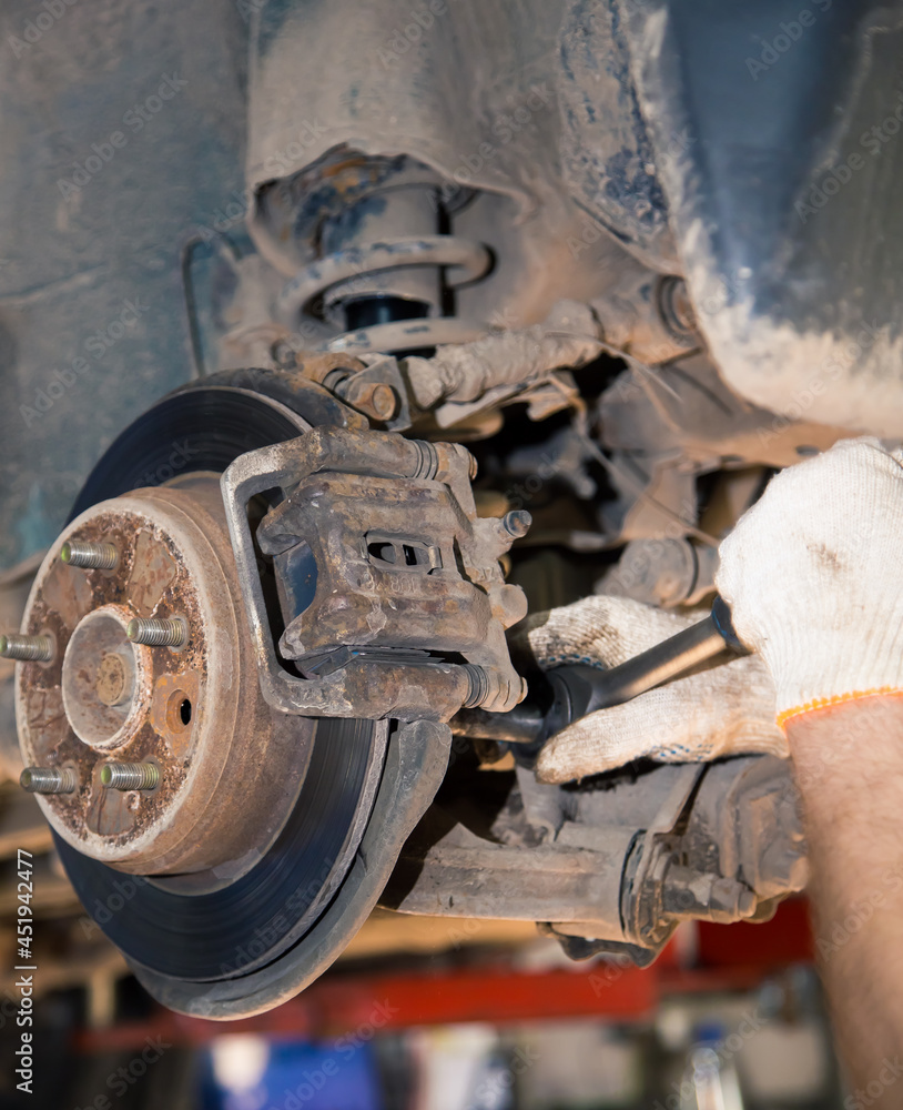 The man's hands unscrew the worn and rusty rear wheel caliper. In the garage, a person changes the failed parts on the vehicle. Small business concept, car repair and maintenance service.