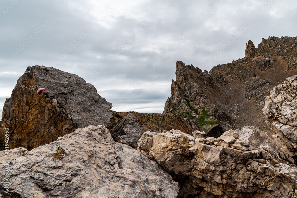 high mountain scenery with rocks, stone with trail mark and cloudy sky in Dolomites