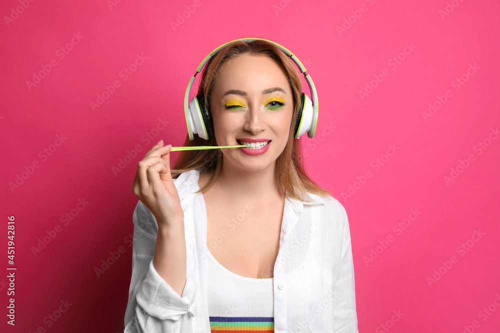 Fashionable young woman with bright makeup and headphones chewing bubblegum on pink background Fashionable young woman with bright makeup and headphones chewing bubblegum on pink background