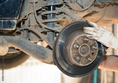 A man's hands are repairing a worn and rusty rear wheel hub. In the garage, a person changes the failed parts on the vehicle. Small business concept, car repair and maintenance service.