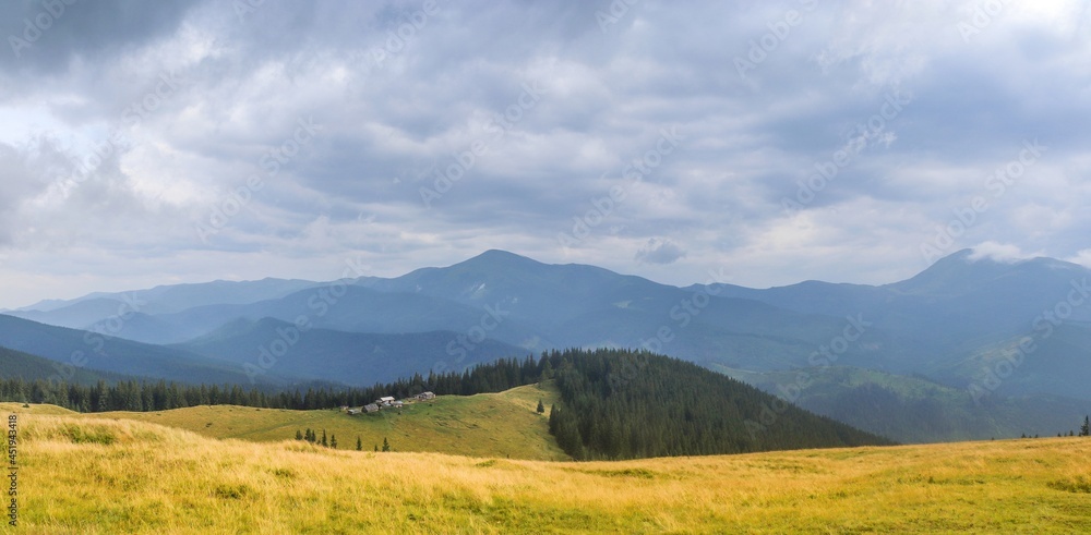 View of hut and summits on the slope of the forest-covered mountains in the Swiss Alps under dramatic clouds on rainy day