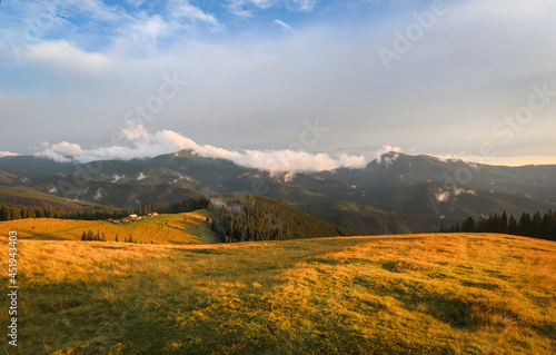 Traditional alpine house and mountain pastures at sunset in summer. Panoramic view on Mountain valley, summits, meadows and colorful sky at sunset in Alp. Mountain landscape with purple sky at dusk.