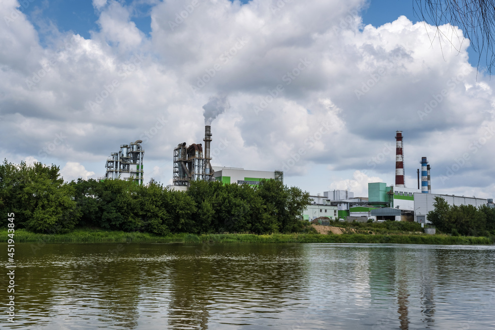 pipes of woodworking enterprise plant sawmill near river. Air pollution concept. Industrial landscape environmental pollution waste of thermal power plant pipes of woodworking enterprise plant sawmill near river. Air pollution concept. Industrial landscape environmental pollution waste of thermal power plant