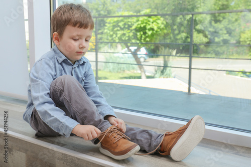 Cute little boy tying shoe laces at home, space for text photo
