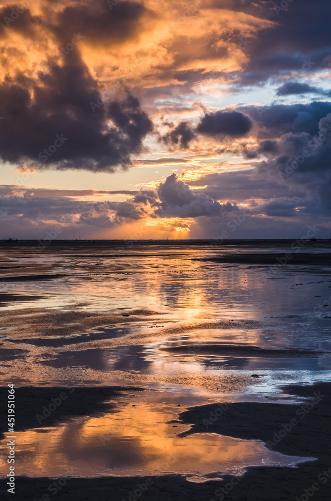 Sunset on a cloudy colorful sky over the North Sea in Denmark with high reflection in the water, vertical