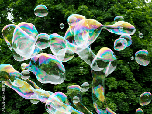 a lot of round soap bubbles are flying in the air against the background of green trees. the festival of soap bubbles in nature in summer. side view