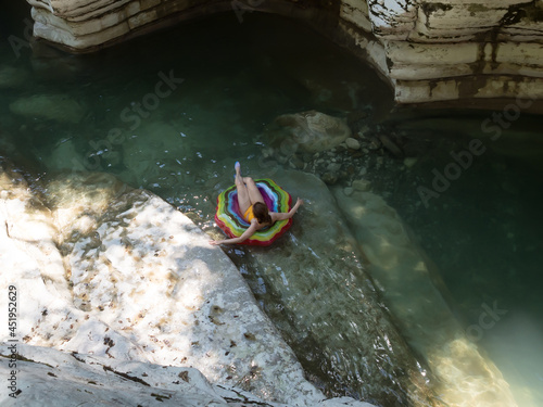 A girl lying on an inflatable swimming ring floats in a calm backwater of a canyon gorge. Top view photo