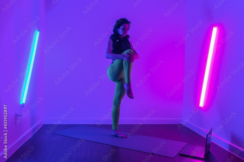 Fit caucasian young woman stretching and looking at the laptop. Studio photo. Colorful sportswear. Stretching. Exercising. High quality photo.