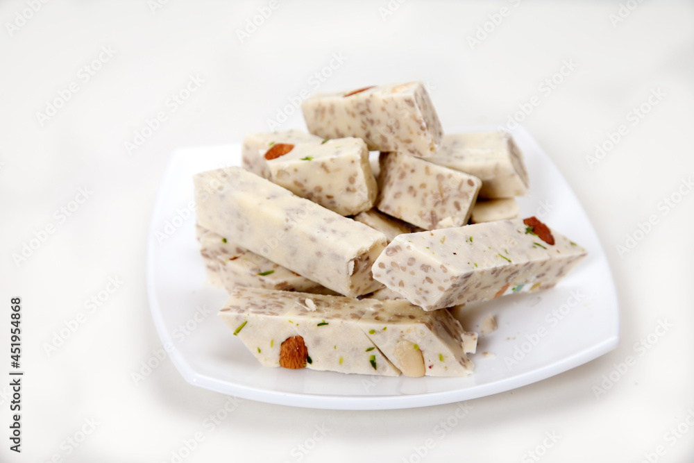 Halva with pistachios and almonds is on a white porcelain plate on a white background.
