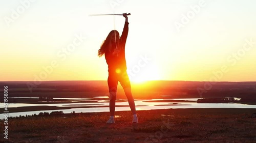 Swords training - young woman with long hair training with two swords on the background of the sunset photo