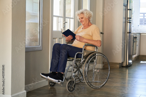 Zufriedene Seniorin im Rollstuhl liest in einem Buch
