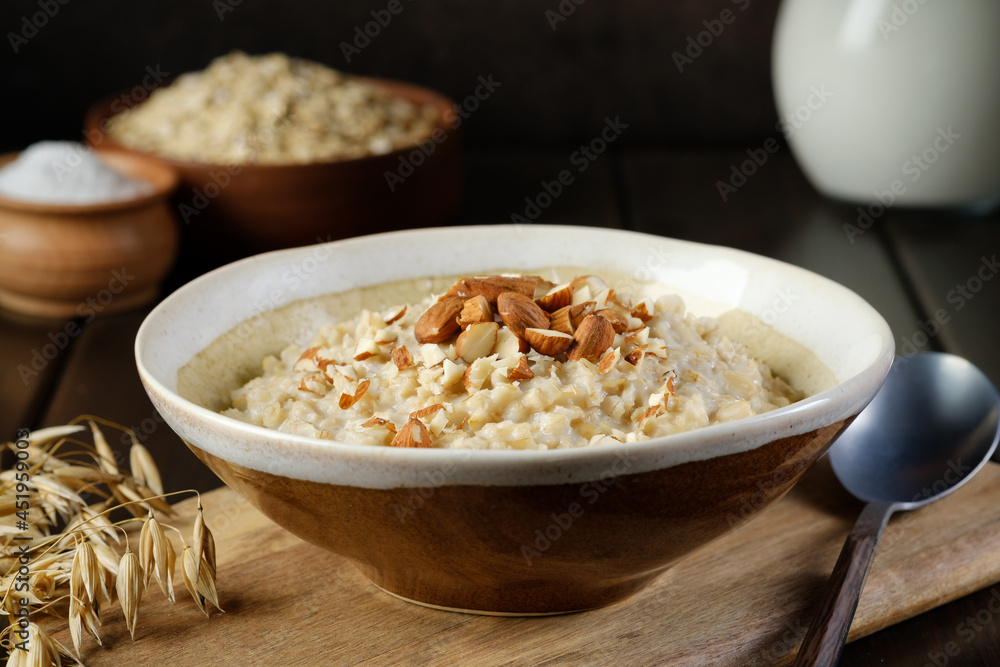 Oatmeal porridge with almonds next to ear of oats lying on the cutting board. Healthy eating. Vegan and vegetarian food. Oatmeal porridge with almonds next to ear of oats lying on the cutting board. Healthy eating. Vegan and vegetarian food.