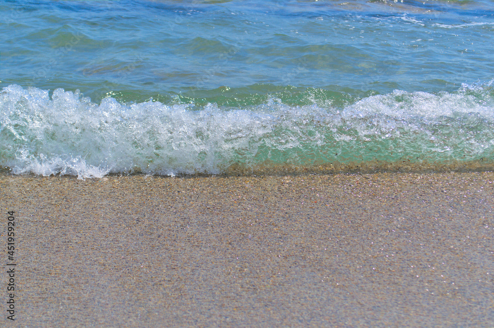 Summer background. Blue sea wave with foam on the sandy shore.