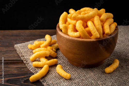 Obraz na plátně Cheese flavored puffed corn snacks on wooden background.