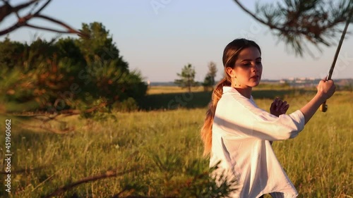 Swords training - young woman waving with a sword on nature at early evening photo