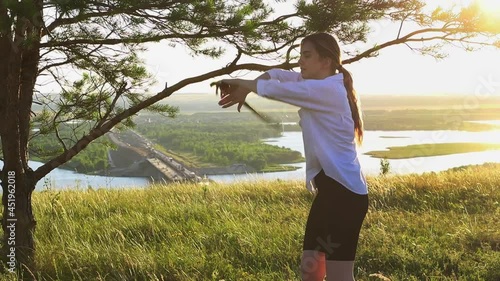 Swords training - young pretty woman in white shirt waving with a sword on nature at early evening - looking in the camera photo