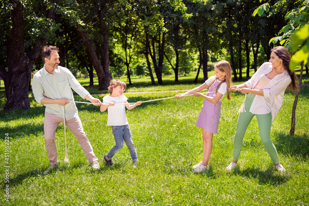 Fototapeta premium Photo of cute charming family dressed casual outfit playing tugging rope smiling outside urban city street
