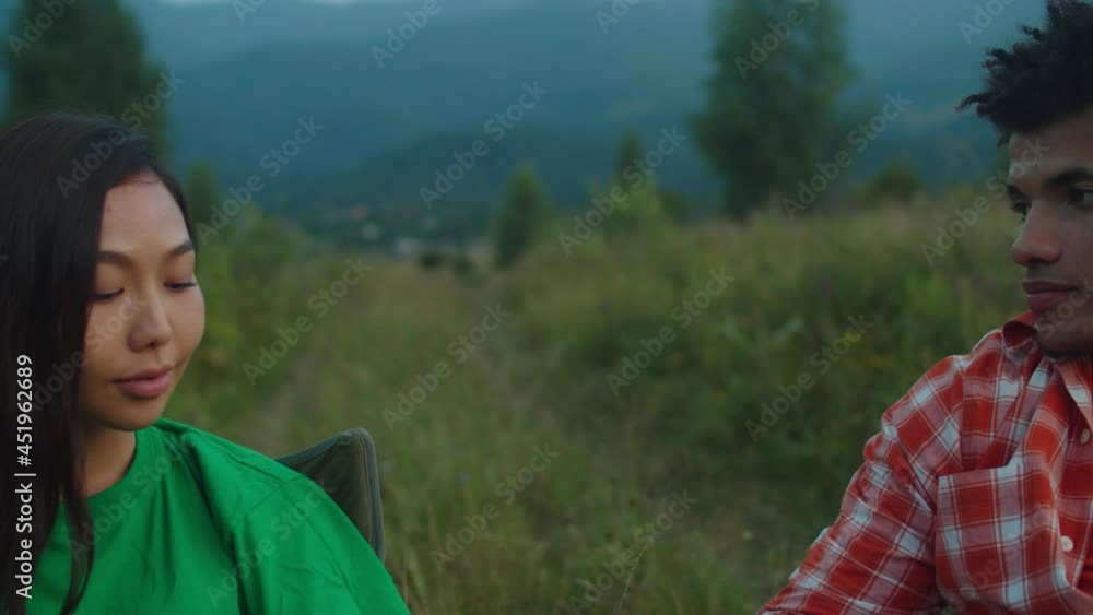 Romantic attractive couple tourists sitting on folded chairs, talking and relaxing with travel mugs of hot drink, enjoying scenic mountain view, freedom and recreation at sunset during mountain hiking Romantic attractive couple tourists sitting on folded chairs, talking and relaxing with travel mugs of hot drink, enjoying scenic mountain view, freedom and recreation at sunset during mountain hiking