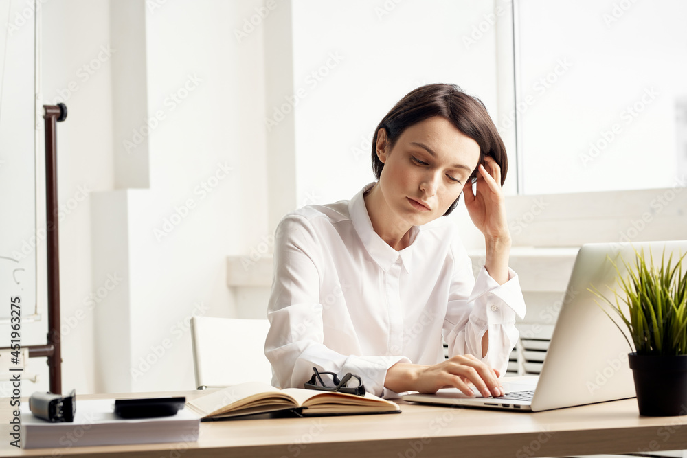 Business woman in white shirt sits at work table in front of laptop office Business woman in white shirt sits at work table in front of laptop office
