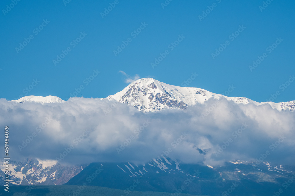 Giant mountains with snow above white clouds in sunny day. Glacier under blue sky. Amazing snowy mountain landscape of majestic nature.