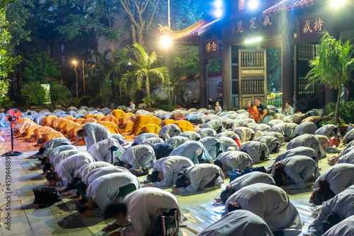 Monks and Buddhists are reverently bowing to Buddha during evening ceremony for Amitabha Buddha at an ancient temple in Ho Chi Minh City, Vietnam