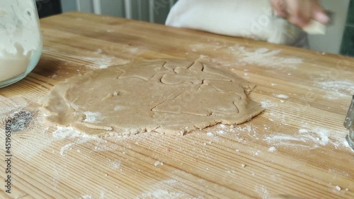 A little girl learns how to make cookies. She uses a template to cut out cookie blanks on the kitchen table. Preparing for the winter holidays.