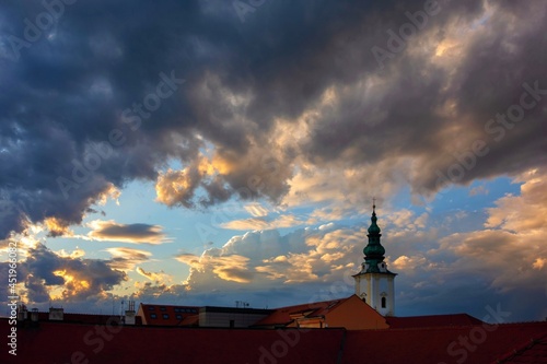 Dramatic stormy and cloudy sky at sunset over roof and church tower in historic city Uherske Hradiste photo