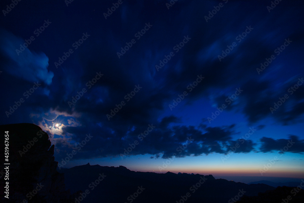 Moon with clouds in the blue hour over the swiss mountains 