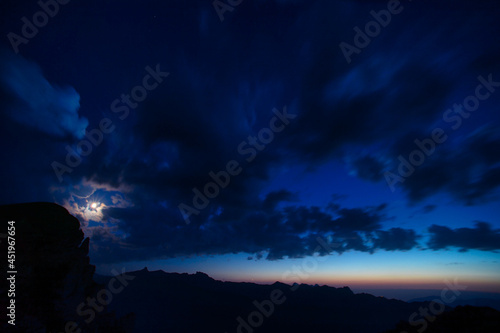 Moon with clouds in the blue hour over the swiss mountains 