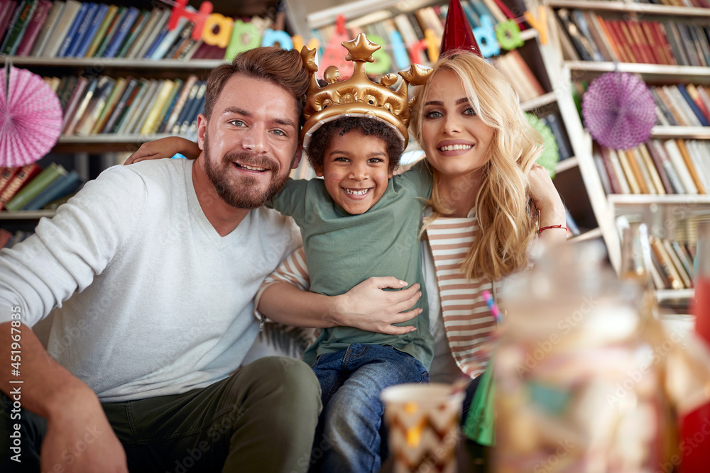 Fototapeta premium Happy couple enjoying a kids birthday party at home with their adopted son. Family, celebration, together