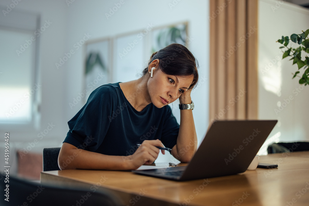 Tired businesswoman looking at laptop while working overtime at home office. Tired businesswoman looking at laptop while working overtime at home office.