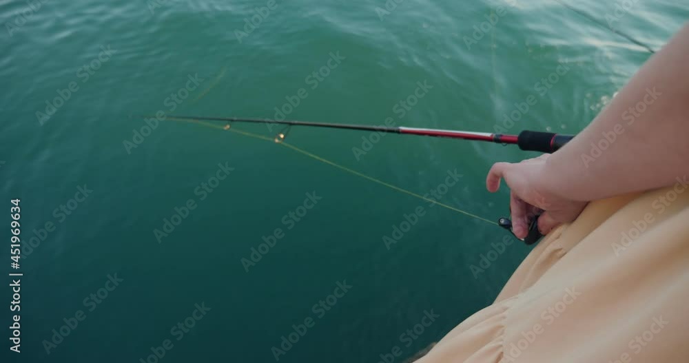 close-up of female hands spinning the reel on the spinning rod. woman fishing. close-up of female hands spinning the reel on the spinning rod. woman fishing.