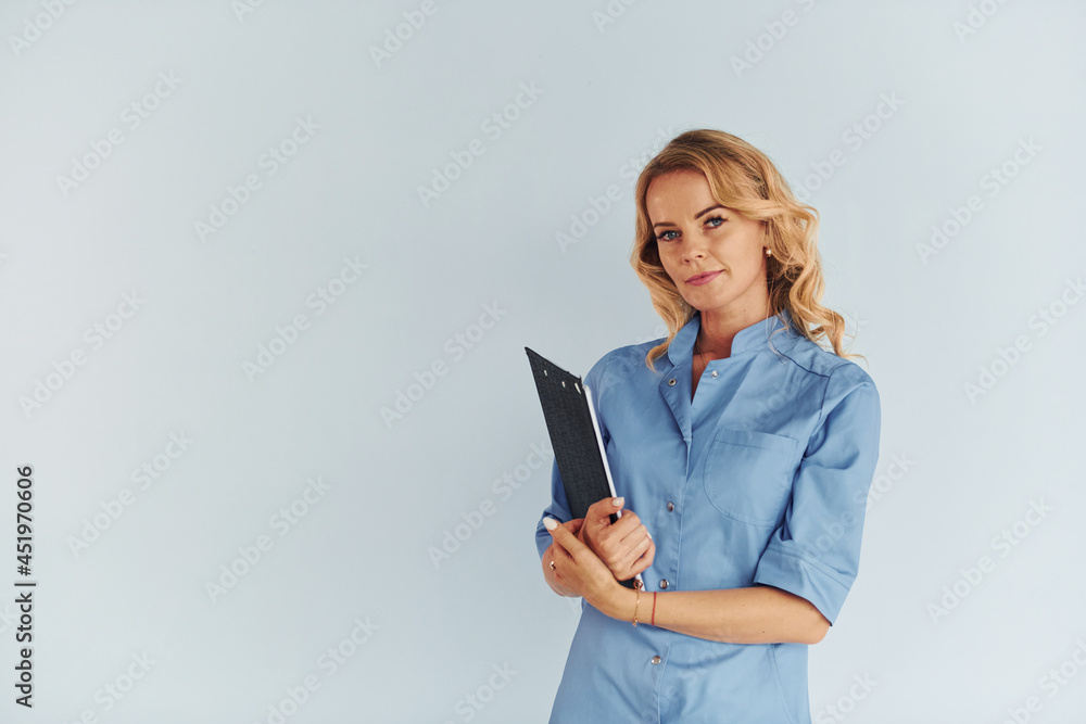 Holding documents. Young female doctor in uniform is indoors Holding documents. Young female doctor in uniform is indoors